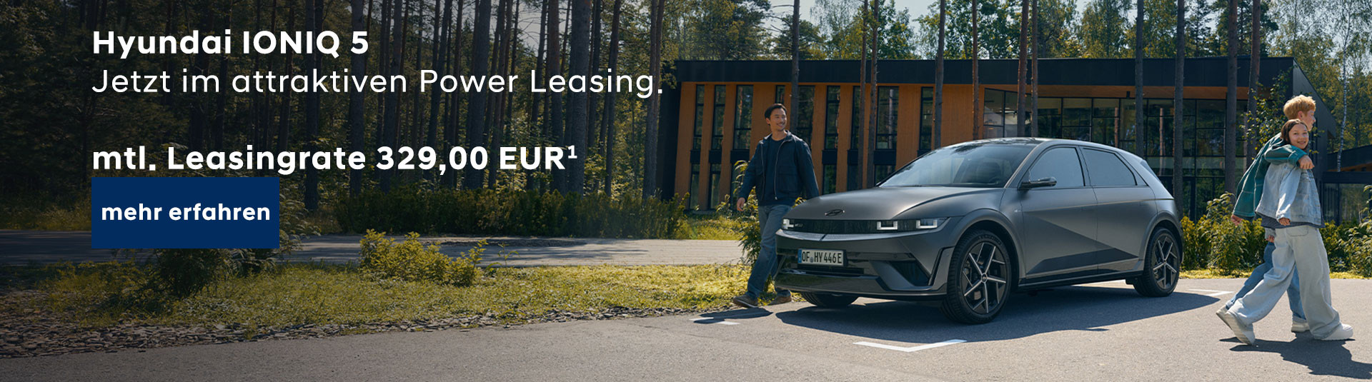 Im Vordergrund steht ein grauer Hyundai IONIQ 5 auf einem Parkplatz vor einem modernen Gebäude mit großen Fenstern und Holzfassade. Links neben dem Fahrzeug steht eine Person mit dunkler Hose und Jacke, die sich mit einer Hand am Auto abstützt. Rechts läuft eine weitere Person in heller Kleidung und Sneakers, beide blicken in Richtung Kamera. Im oberen linken Bereich ist weißer Text zu sehen: 'Hyundai IONIQ 5 Jetzt im attraktiven Power Leasing. mtl. Leasingrate 329,00 EUR¹'. Unten links befindet sich ein blauer Button mit weißer Schrift: 'mehr erfahren'. Im Hintergrund sind Bäume und Grünflächen sichtbar.