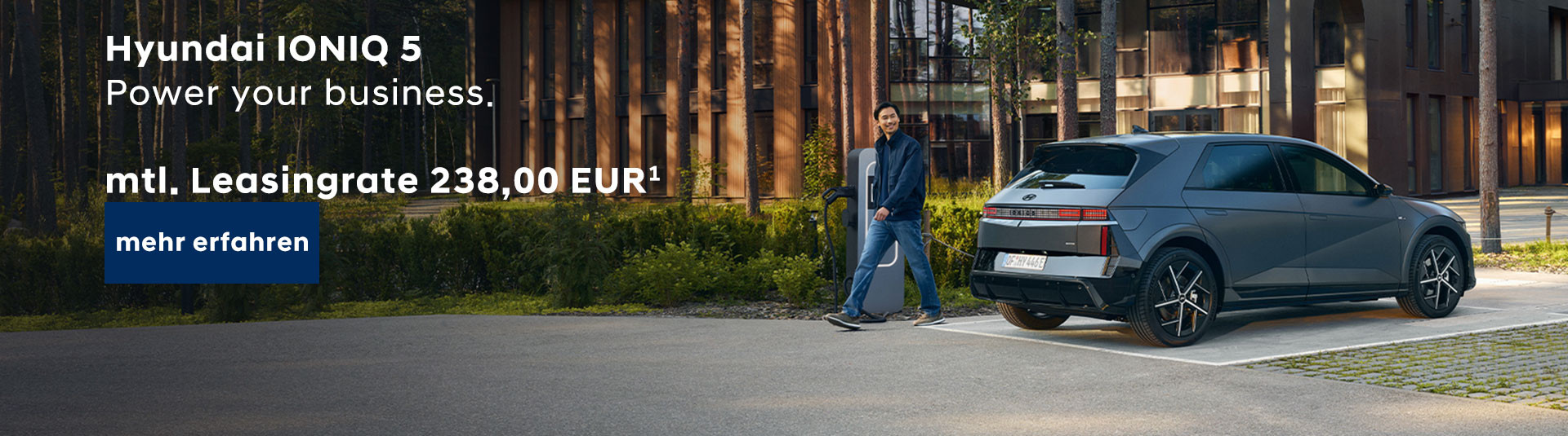 Ein Mann im Anzug steht neben einem silbernen Hyundai IONIQ 5, der auf einem Parkplatz vor einem modernen Bürogebäude abgestellt ist. Der Mann hält einen Aktenkoffer in der linken Hand und blickt in Richtung Kamera. Links oben im Bild steht weißer Text auf dunkelblauem Hintergrund. Ein blauer Button mit weißer Schrift befindet sich darunter.
